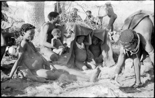 Group of children under a kaross, Debe sitting in his father's lap, and /Naoka and Di!ai sitting