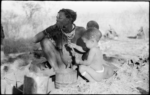 Debe sitting on Di!ai's knee and taking a knife out of a sheath