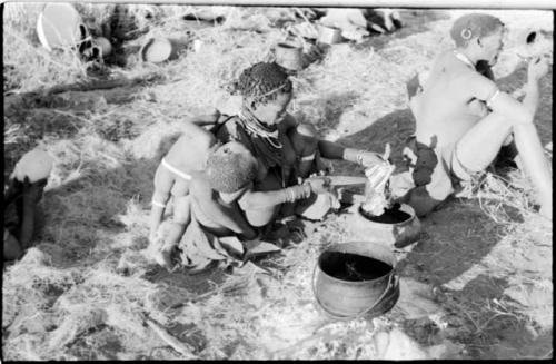 Di!ai cutting meat and putting it in a pot, with Debe leaning against her, and !U sitting beside her