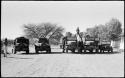 Men standing and sitting on and next to expedition trucks lined up