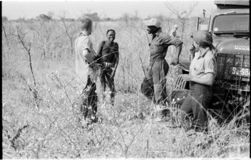 /Gunda (N!ai's husband) standing near expedition truck with Kernel Ledimo, Elizabeth Marshall Thomas, and John Marshall