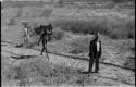 Two men walking with Wilhelm Camm and carrying his belongings