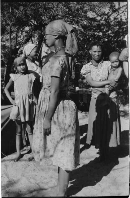 Woman in a dress standing, profile, with other people standing behind her