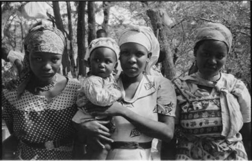 Three women standing, one holding a baby