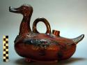 Brown glazed pottery duck (with designs on body). Handle and dorsal aperture.