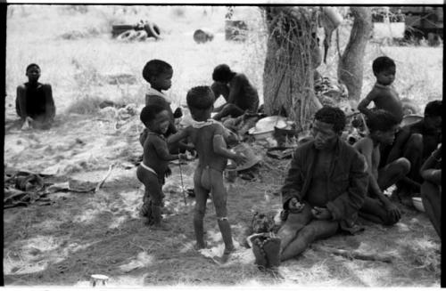 ≠Toma wearing a coat and a group of standing children including Debe ("Gao Medicine's" and Di!ai's son), /Gaishay, !Ungka Norna, Bau to the right, and other unidentified people