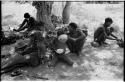 Group of people including two unidentified people to the left, ≠Toma lying down and wearing a coat, !Unkga Norna, an unidentified boy drinking from a bowl, "Crooked /Qui," and /Gaishay ("Gao Medicine's" and /Naoka's son)