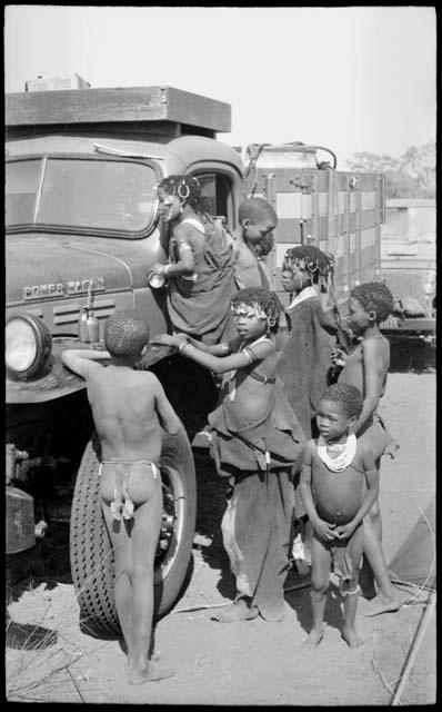 Children beside an expedition truck including N!ai wearing a kaross