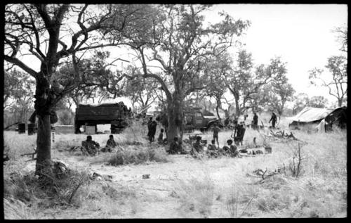 Group of Ju/'hoansi with expedition trucks and expedition camp in the background