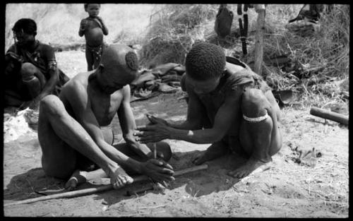 Dam and ≠Gao creating a fire with firesticks; unidentified people in the background