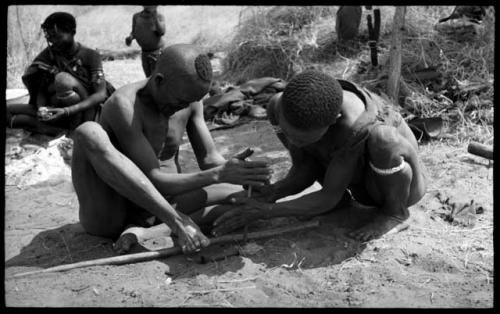 Dam and ≠Gao creating a fire with firesticks; unidentified people in the background