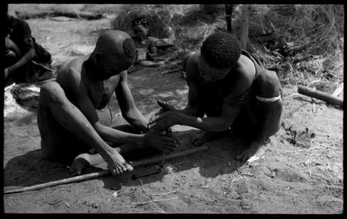 Dam and ≠Gao creating a fire with firesticks; unidentified people in the background