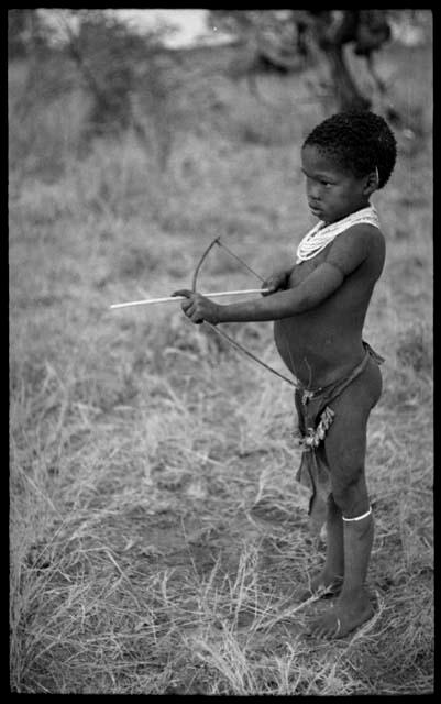 /Gaishay ("Gao Medicine" and Di!ai's son) with a toy bow and arrow, pulling back the string to release an arrow