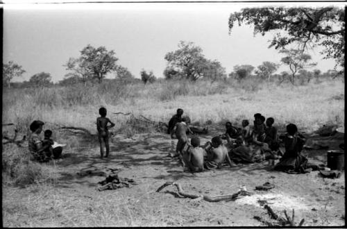 Women and children sitting in the shade while Elizabeth Marshall Thomas holds a child, distant view