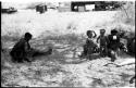 Khuan//a sitting to the left, her youngest son ≠Toma standing with an unidentified girl, and two unidentified women with the expedition camp in the background