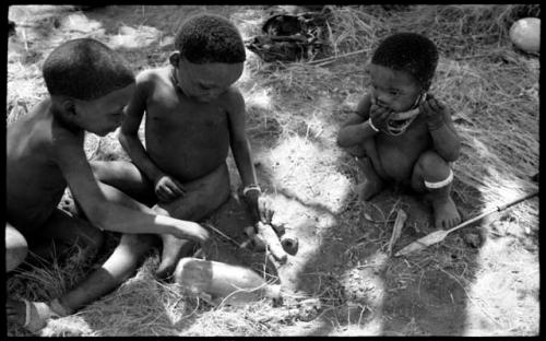 Unidentified boy to the left, "Little ≠Gao" playing with a handmade toy automobile made from veldkos, and Debe ("Gao Medicine" and Di!ai's son) eating something