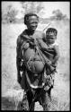 Khuan//a with her son, ≠Toma, tied in her kaross, wearing dance rattles