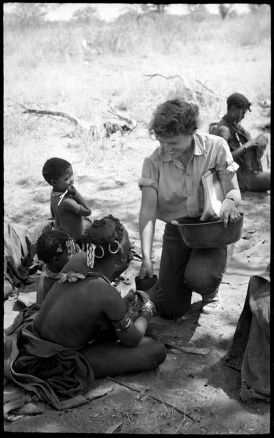 Elizabeth Marshall Thomas giving tobacco to an unidentified woman; other unidentified people in the background