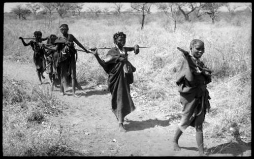 Girls walking in a line including an unidentified, visiting girl in the front, another unidentified girl, !Ungka's cousin, and several younger girls