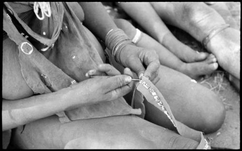 Woman's hands sewing beads onto a leather strip, close-up