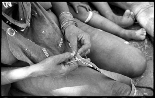 Woman's hands sewing beads onto a leather strip, close-up