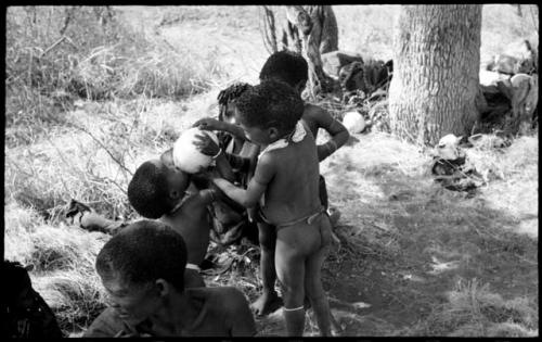 Group of unidentified children including /Gaishay helping his younger brother, Debe, take a drink from an ostrich eggshell