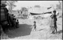 Children playing around the expedition truck while Di!ai and Debe walk away; the expedition camp is in the background