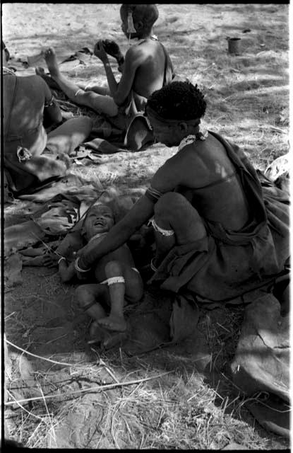 Di!ai sitting and reaching to pick up her son, Debe, with unidentified people in the background