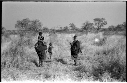 Di!ai walking from the back with Debe sitting on her shoulder while /Gaishay runs ahead; another unidentified woman is walking beside her