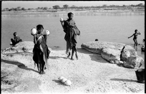 Two women standing beside Nama Pan holding ostrich egg shells with unidentified people in the background