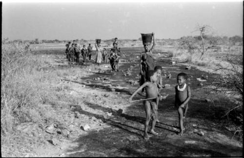 Women and children returning from Nama Pan with water; Di!ai and !Ungka carrying buckets on their heads, distant view