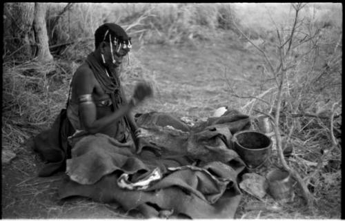 Woman pounding bone and red powder in her kaross with a stone