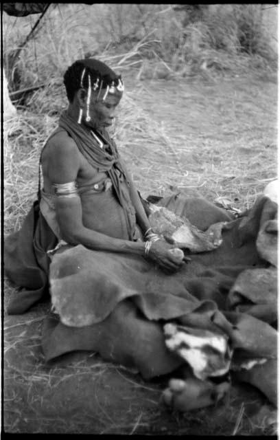 Woman pounding bone and red powder in her kaross with a stone