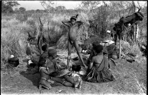 Group sitting in a werft by a fire; left to right: "Old /Gasa," Dam ("Old /Gasa's" son-in-law; ≠Gisa's husband) playing a //guashi, an unidentified girl kneeling next to him, a woman, mostly likely /Goishay, and ≠Gao ("Old /Gasa's" son; Gau's brother)