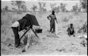 John Marshall filming "/Gao Music" sitting and playing the //guashi and Kernel Ledimo standing to the side