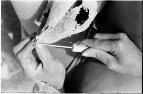 Person sewing, close-up of hands using awl to make a hole for putting a cord through