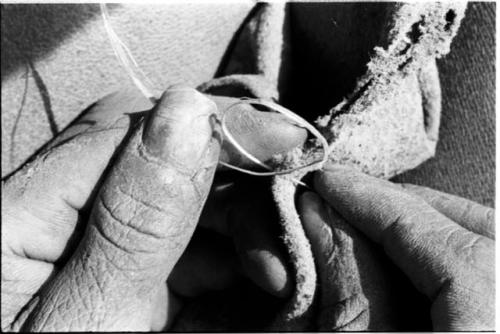 Person sewing, close-up of hands putting unrolled vegetable fiber through a hole in leather