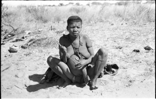 Tsekue seated, making rhythmic sounds with grass stems