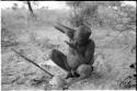 Oukwane drinking, using one hand to squeeze juice into the palm of the other hand, full figure