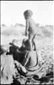 N!whakwe standing on his mother Tsekue's shoulder, seen from behind