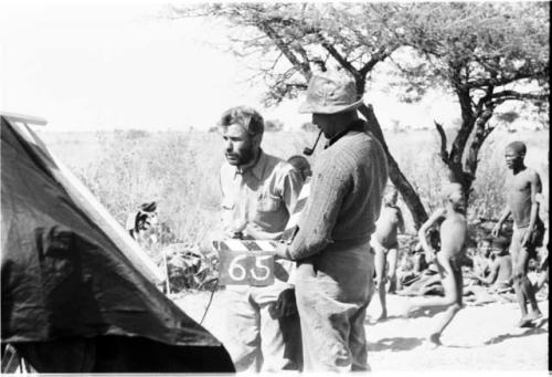 Daniel Blitz and Casper Kruger demonstrating how to put numbers on a camera roll, with a group of people standing and sitting in the background