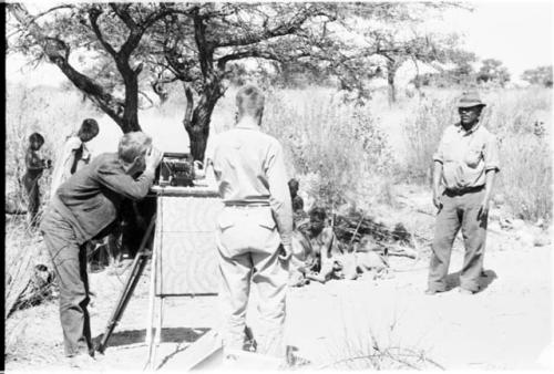 John Marshall setting up sound sync with Daniel Blitz and Wilhelm Camm standing nearby; group of people in the background (print is a cropped image)