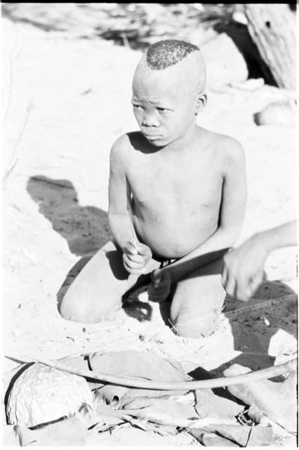 /Gaiamakwe striking a rhythm on the lower string of musical bow with a stick