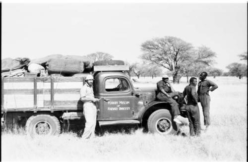 Expedition truck with sign painted on side reading "Peabody Museum of Harvard University," with Robert Story, Kernel Ledimo, /Gishay, and Simon Molamo gathered around