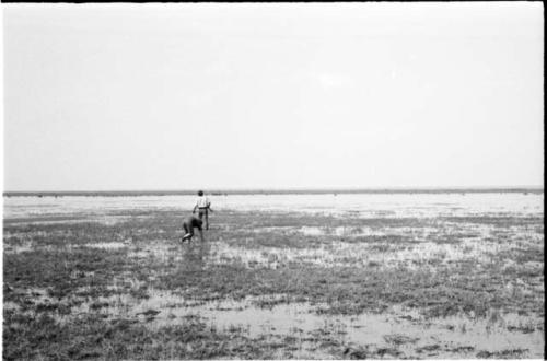 Elizabeth Marshall Thomas and John Marshall, who is holding a gun in his hand, wading in Lake Ngami