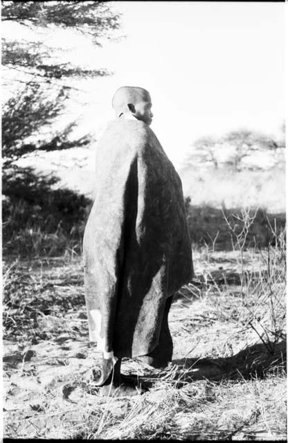 Visiting man wrapped in a big kaross, seen from behind, full figure standing