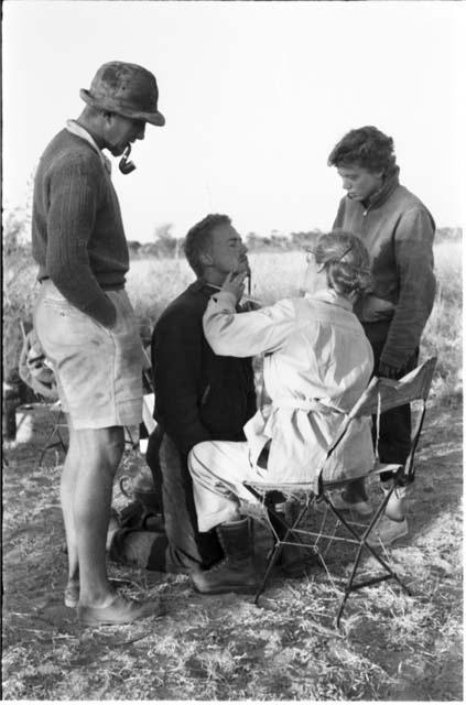 Lorna Marshall trimming John Marshall's beard, with Casper Kruger and Elizabeth Marshall Thomas advising, full figure