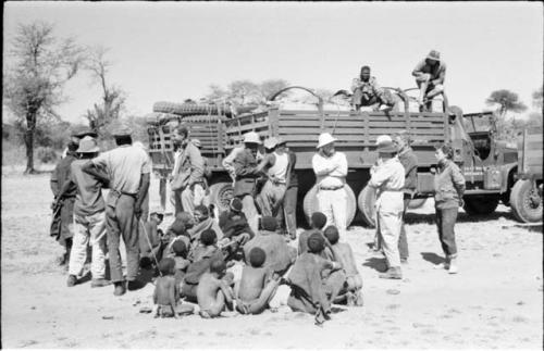 People sitting and standing next to expedition members and trucks