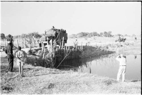 GMC truck crossing a bridge, with expedition members watching, seen from a distance