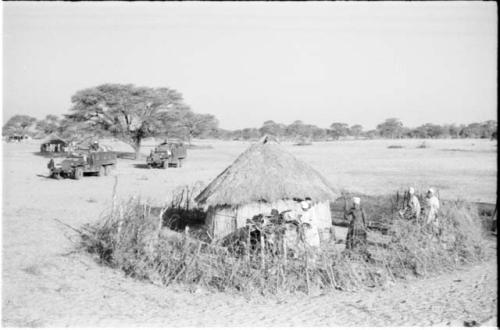 Women gathered around a hut, with the expedition trucks in the background